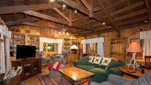 Interior acogedor de una cabaña con techo de madera, un televisor, un sofá verde y una chimenea.