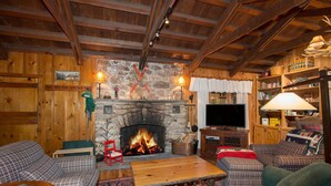 Una sala de estar acogedora con chimenea de piedra, muebles a cuadros y un televisor.