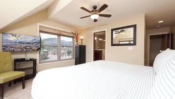 Une chambre à coucher comprenant un lit, un ventilateur de plafond, une télévision, une fenêtre avec vue et une commode.