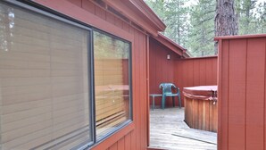 A wooden deck with a hot tub and a chair, a large window, and a wooden fence. - 8 Leisure - Light & Bright Home, Hot Tub, Quiet Area Close to SHARC + Passes Included (Sunriver)