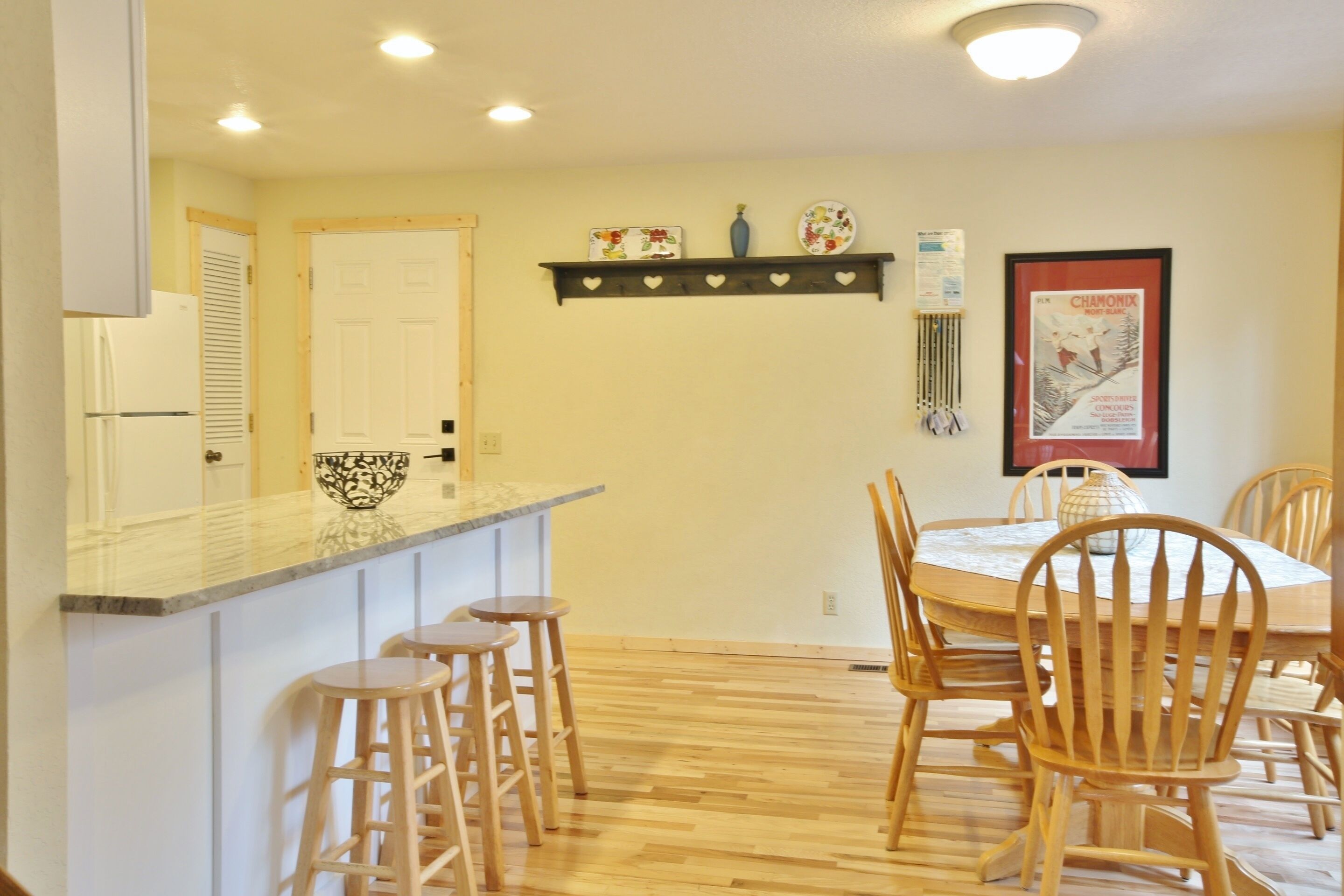 A kitchen with a wooden floor, a white refrigerator, a marble countertop, and a dining area with wooden chairs and a table.