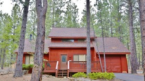 A two-story cabin with a red exterior, a front porch, and a garage. - 8 Leisure - Light & Bright Home, Hot Tub, Quiet Area Close to SHARC + Passes Included (Sunriver)