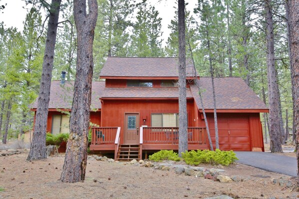 A two-story cabin with a red exterior, a front porch, and a garage.