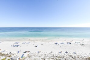 Une vaste plage avec une eau d’un bleu limpide, du sable blanc et plusieurs parasols.