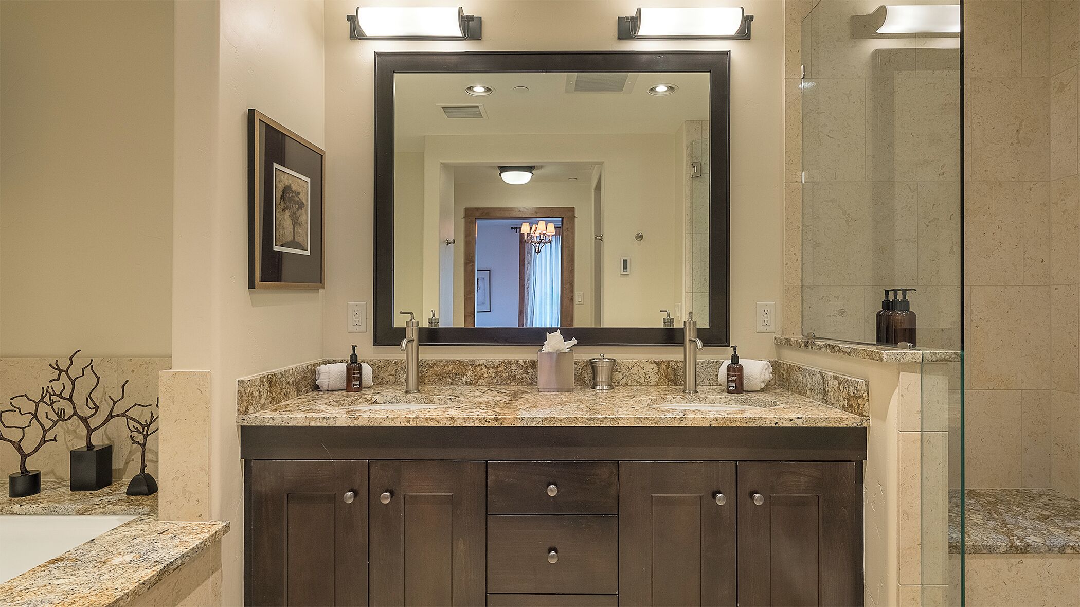 A bathroom with a large mirror, double sink vanity, and a shower area.