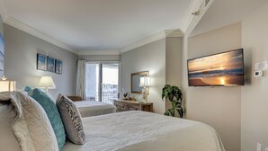 A hotel room with a large bed, a television, a desk, and a balcony with a view of the ocean.