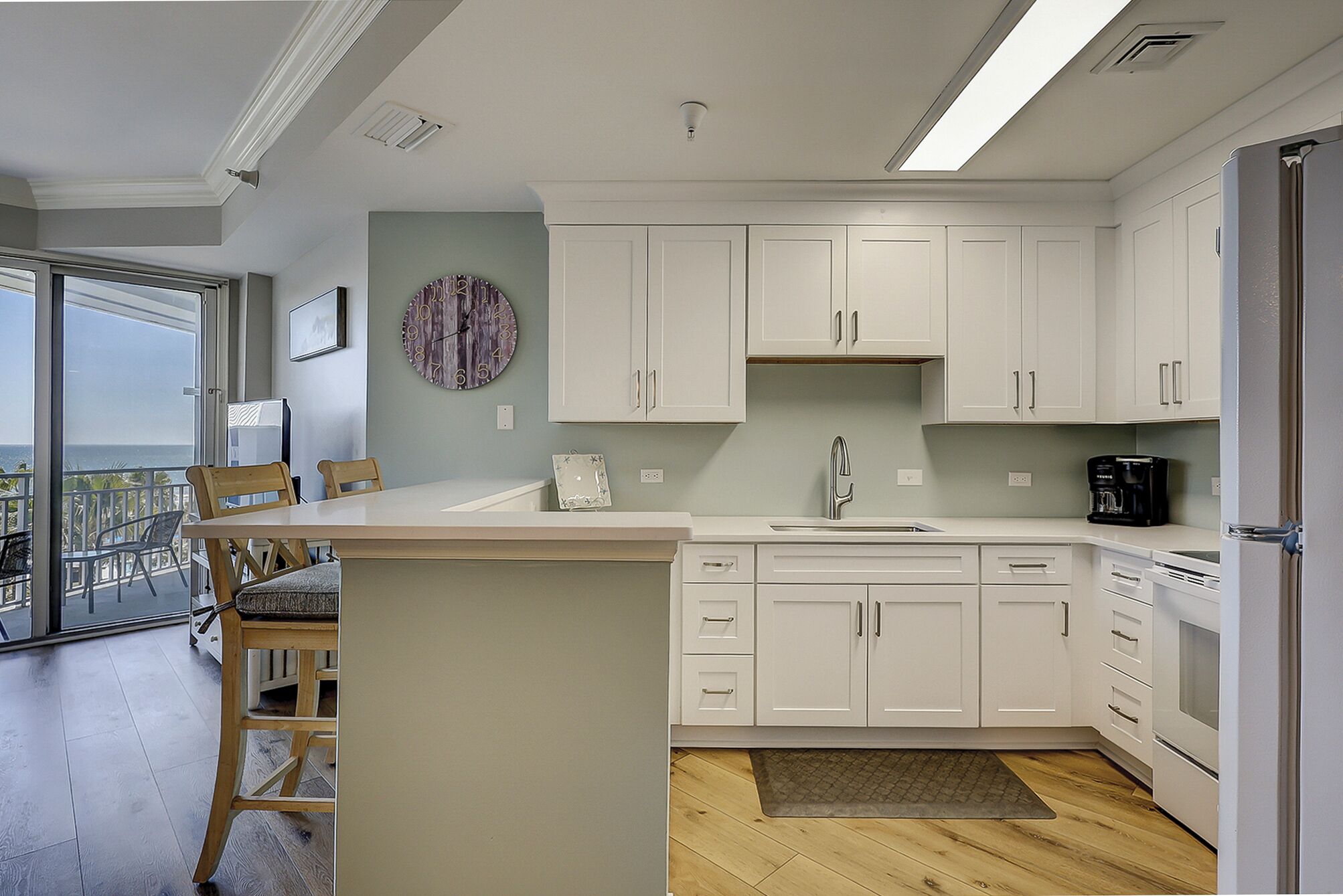 A modern kitchen with white cabinets, a built-in island, and a view to the outside.