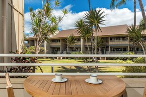 A wooden deck with two white cups on saucers, overlooking a building with multiple balconies and palm trees.