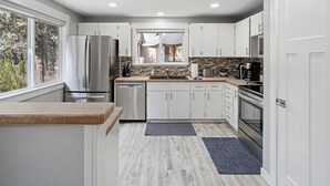 Una cocina moderna con armarios blancos, un refrigerador de acero inoxidable, un lavavajillas, una cafetera y un amplio ventanal.