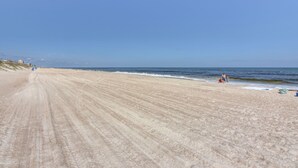 En bred sandstrand med milda vågor, en klar himmel och några få personer på avstånd.