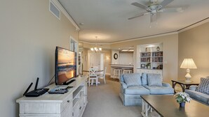 A living room with a TV, sofa, coffee table, and a dining area with chairs and a chandelier. - 2315 Windsor II -Beautiful Oceanfront 1 Bedroom Villa! (Hilton Head Island)