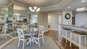 A spacious kitchen with a dining area, featuring a large island with stools, a chandelier, and a clock on the wall. - 2315 Windsor II -Beautiful Oceanfront 1 Bedroom Villa! (Hilton Head Island)