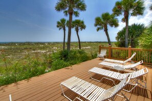 Relax on the deck with comfortable lounge chairs overlooking lush vegetation and palm trees.