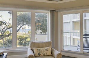 Enjoy a serene view of the sea from this inviting room, featuring a large window and a comfortable armchair.