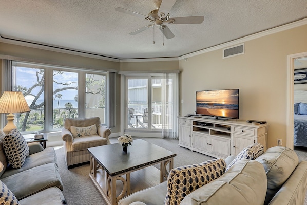 Relax in a spacious living room with a large window offering a view of the outdoors, a ceiling fan, and a flat-screen TV.