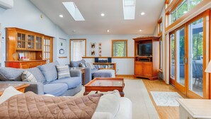 A spacious living room with a sofa set, a coffee table, and a television. There is a wooden cabinet with a TV stand, and a large window with a view of the outdoors. - The Willows:"Delightful Cottage with Peaceful Sunsets" (Lodi)