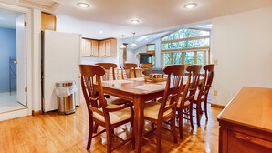 A spacious dining area with a wooden table and chairs, a trash can, and a view of the outdoors through large windows. - The Willows:"Delightful Cottage with Peaceful Sunsets" (Lodi)