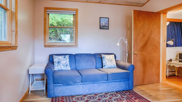 A blue sofa with patterned cushions, a small white side table, a framed picture of Finger Lakes, and a patterned rug on a wooden floor.