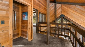 Een houten interieur met een hoge plafond, een trap en een deur die naar een andere kamer leidt.