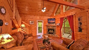 Un interior acogedor de cabaña con chimenea, paredes de madera, televisor y una zona de estar confortable.