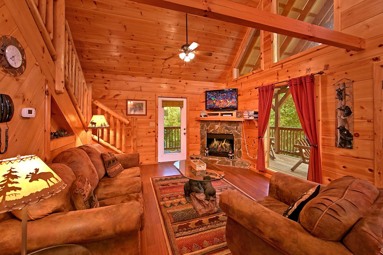 A cozy cabin interior with a fireplace, wooden walls, a television, and a comfortable seating area.