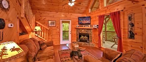 A cozy cabin interior with a fireplace, wooden walls, a television, and a comfortable seating area.