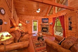 A cozy cabin interior with a fireplace, wooden walls, a television, and a comfortable seating area.