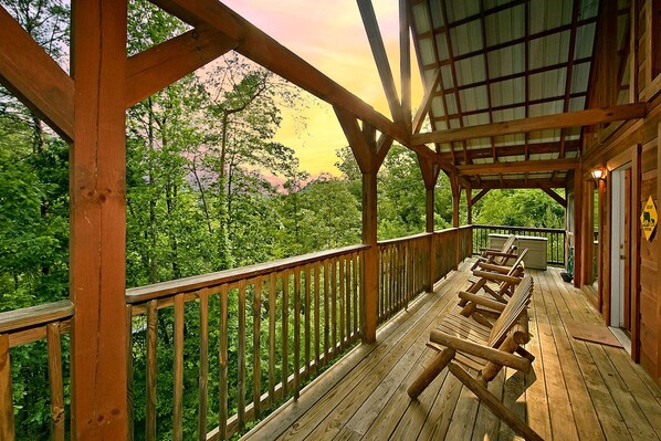 A wooden deck with benches, a covered area, and a view of a forested landscape.