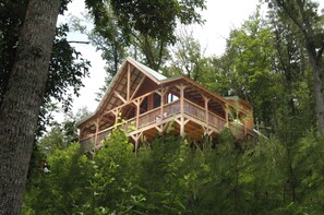 Una cabaña de madera con balcón, rodeada de un bosque denso.