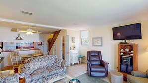 A living room with a floral sofa, a leather armchair, a TV, and a wooden cabinet with audio equipment.