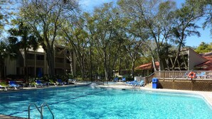 A swimming pool with clear blue water, surrounded by lounge chairs and trees.