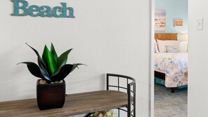 Une pièce avec un lit, une petite table sur laquelle est posée une plante en pot, et un mur orné d’un panneau indiquant « Plage ».