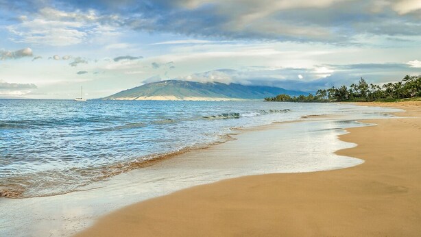 Une plage avec un bateau sur l’eau, une montagne en arrière-plan et un ciel dégagé.