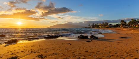 A beach with footprints leading to the water, a sunset in the background, and a clear sky.