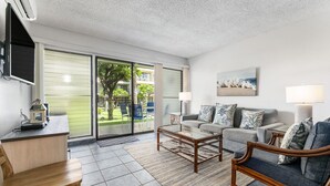 Un salon moderne comprenant un canapé, un fauteuil, une table basse et un téléviseur fixé au mur.