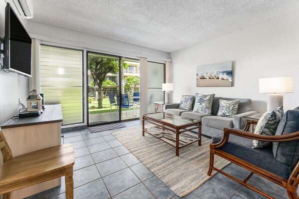 A modern living room with a sofa, armchair, coffee table, and a TV mounted on the wall.
