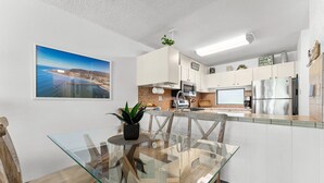 Une cuisine moderne avec des meubles blancs, une table à manger en verre et une vue sur la plage.