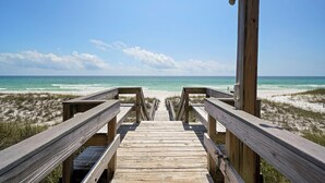 Une promenade en bois qui mène à une plage d’où l’on a une vue dégagée sur l’océan et le ciel.