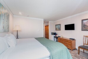 Habitación de hotel con cama, escritorio, silla, televisor y un cuadro en la pared.