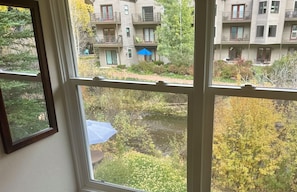 Vista desde una ventana de una zona residencial con un pequeño arroyo, un paraguas azul y edificios de varios pisos con balcones.