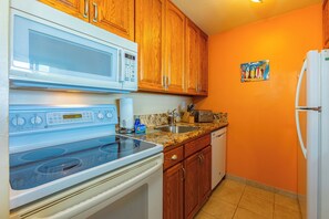 Une cuisine avec des meubles de rangement en bois, un micro-ondes blanc, une cuisinière, un évier et un réfrigérateur.