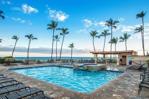 A swimming pool with lounge chairs and palm trees, overlooking the ocean.