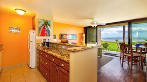 Una cocina con vista al océano, armarios de madera, encimeras de granito y un comedor con sillas.