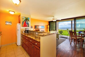 A kitchen with wooden cabinets, a granite countertop, and a view of the ocean through large windows.