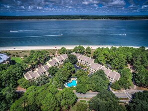 An aerial view of a coastal resort with multiple bungalow-style buildings, a central swimming pool, and a beach in the background. - 1468 Sound Villas- Coastal Chic and Calibogue Sound Views (Hilton Head Island)