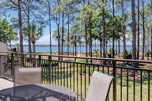 A balcony with a view of a lake, surrounded by tall trees and equipped with outdoor furniture. - 1468 Sound Villas- Coastal Chic and Calibogue Sound Views (Hilton Head Island)