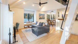 Uma sala de estar moderna com um sofá cinzento, piso de madeira, um ventilador de teto e um espaço de jantar com mesa e cadeiras.
