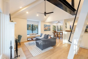 A modern living room with a grey sofa, wooden flooring, a ceiling fan, and a dining area with a table and chairs.