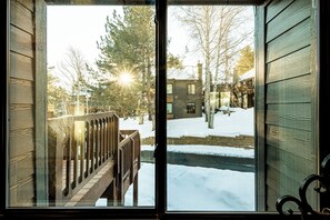 A wooden deck with a railing, a snow-covered ground, and a view of a building with a chimney.
