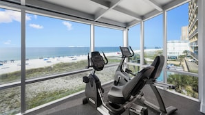 Une salle de sport équipée de matériel d’exercice et offrant une vue sur la plage et l’océan.